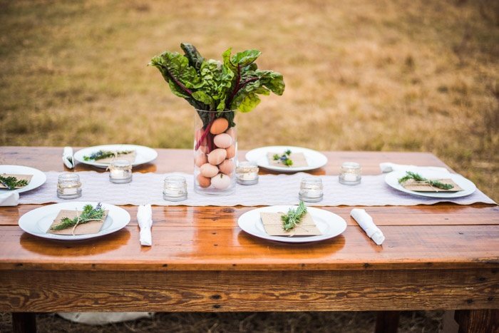 Farm to table display with swiss chard and eggs. Glass vase and place settings with rosemary and lavander tied to menu